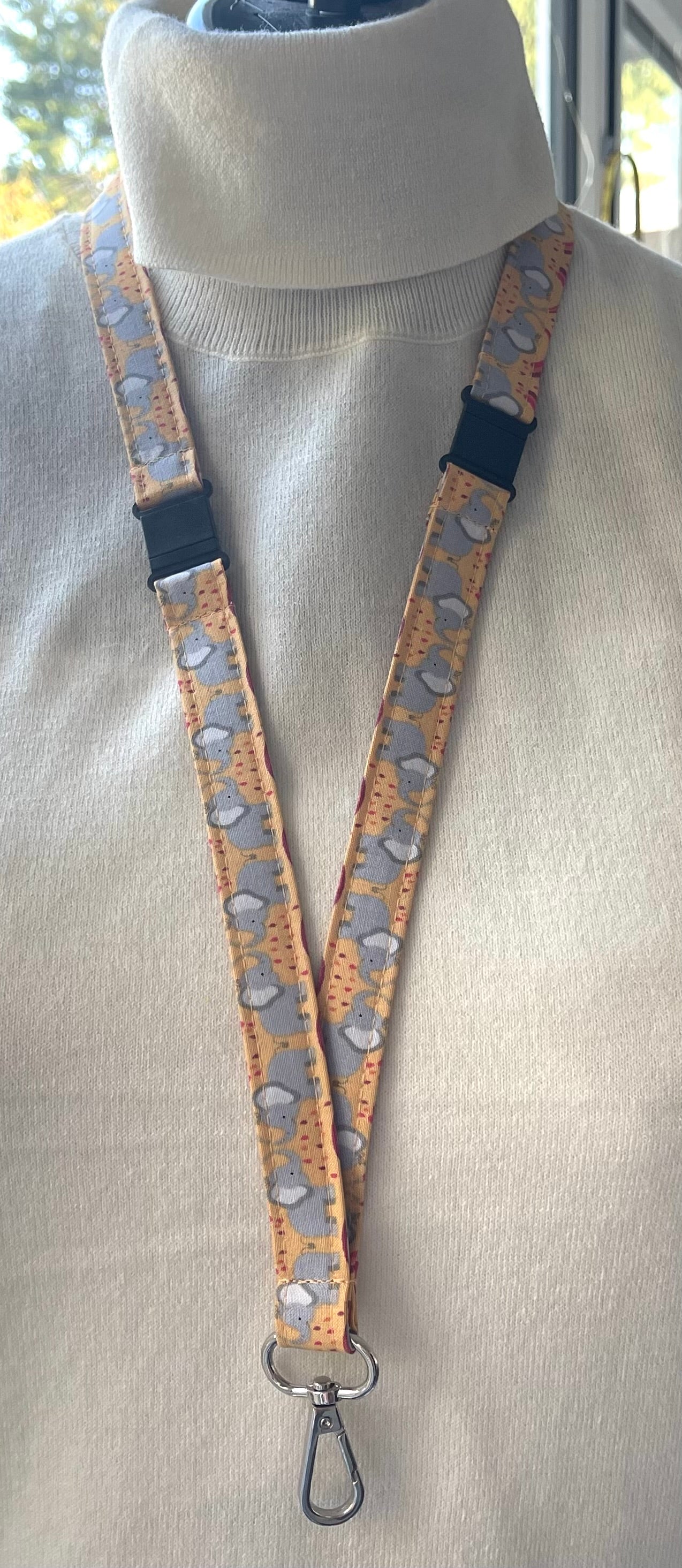 A fabric lanyard with an elephant pattern displayed on a mannequin's neck.
