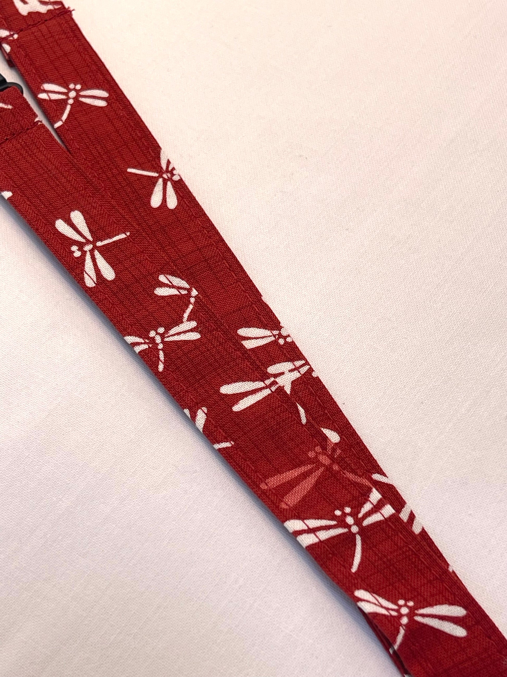 Red lanyard with white dragonfly pattern on a light beige background
