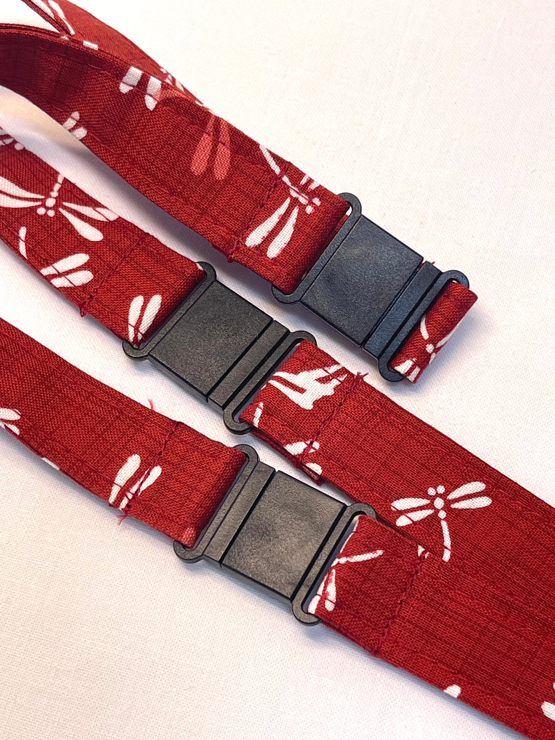 Red lanyard with white dragonfly pattern and black plastic breakaway clip on a light background