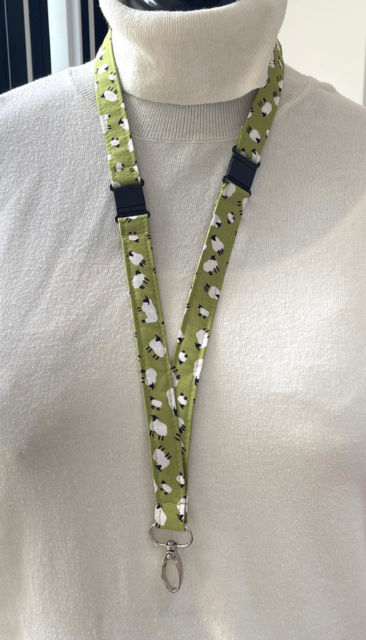 Lanyard with a pattern of small white sheep on a green background, worn around a mannequin neck.