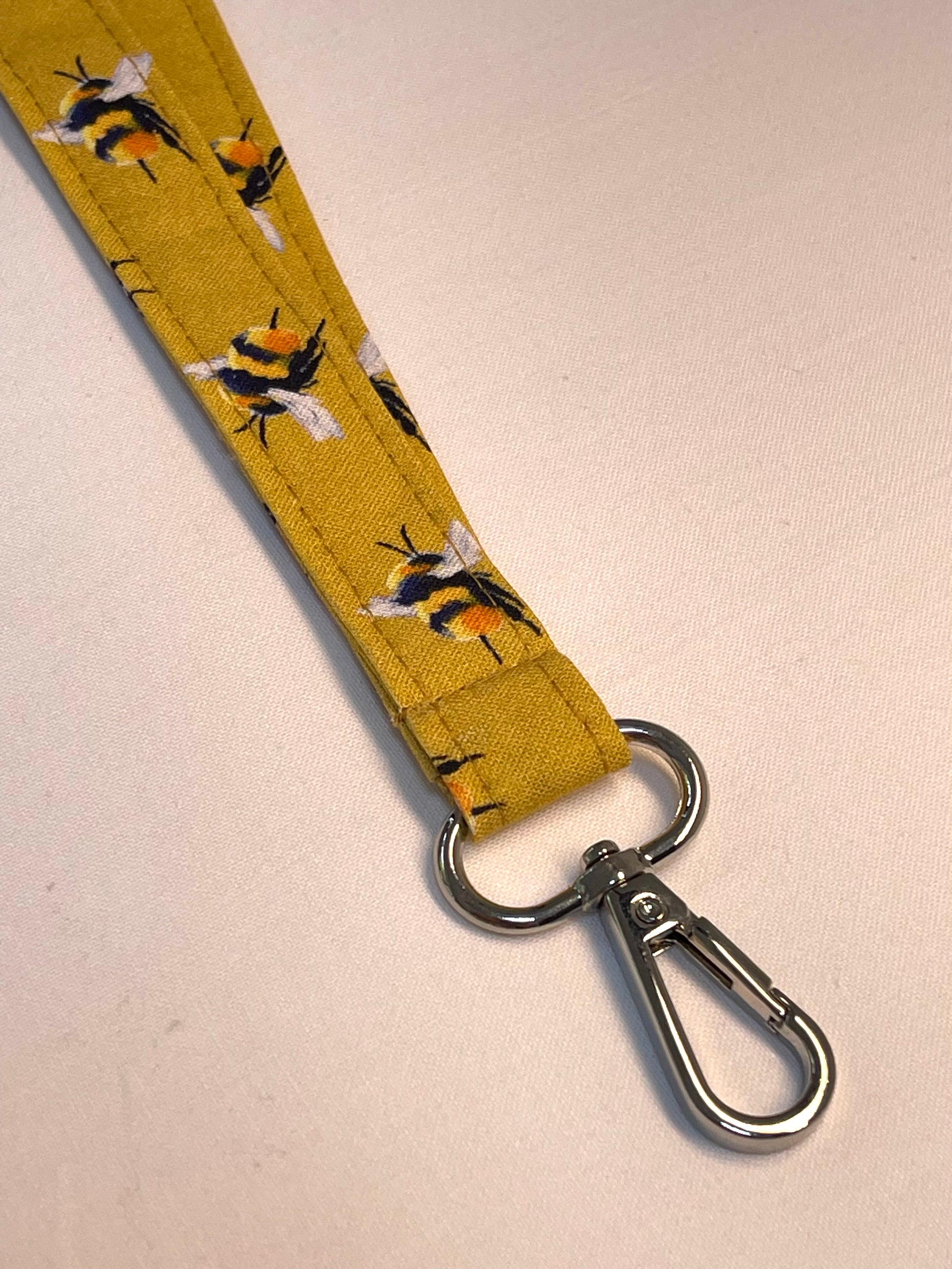 Yellow lanyard with bee pattern and metal clip on a beige background