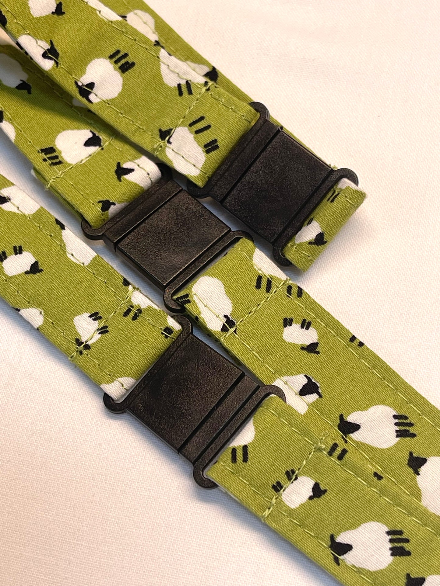Green lanyard with sheep pattern and black buckle on a beige background