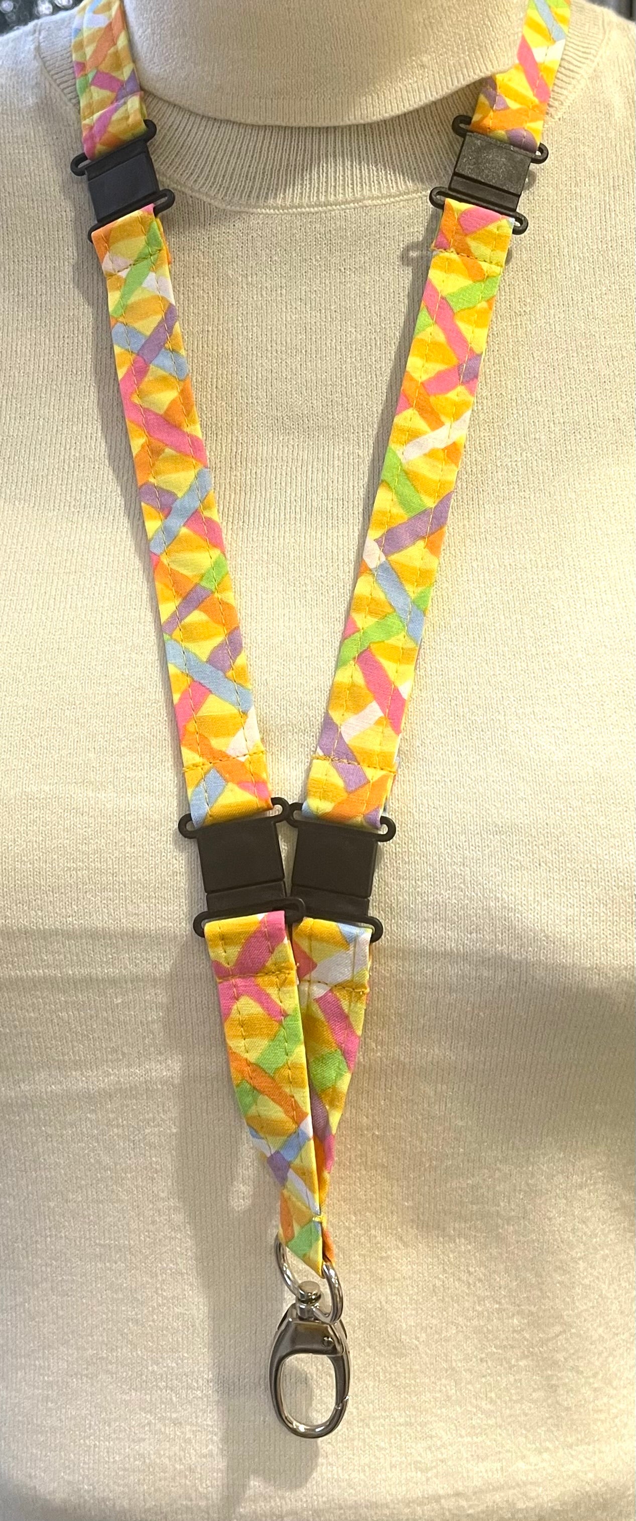 A colorful confetti-patterned lanyard with black straps and a plastic D-ring clip, displayed on a mannequin.