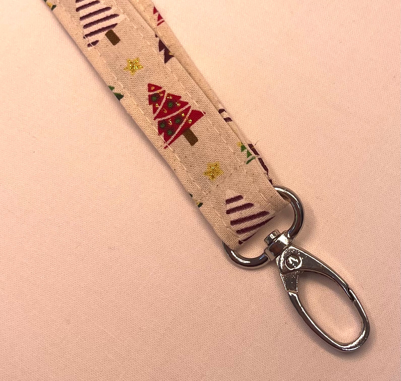 Fabric lanyard with Christmas tree pattern and metal clip on a pink background