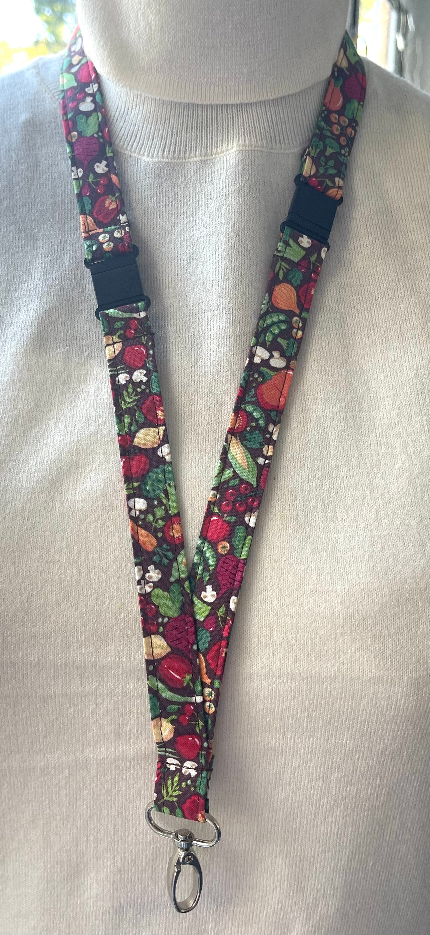 A fabric lanyard with a floral pattern, featuring a safety breakaway clip and a metal ID holder, displayed on a mannequin.