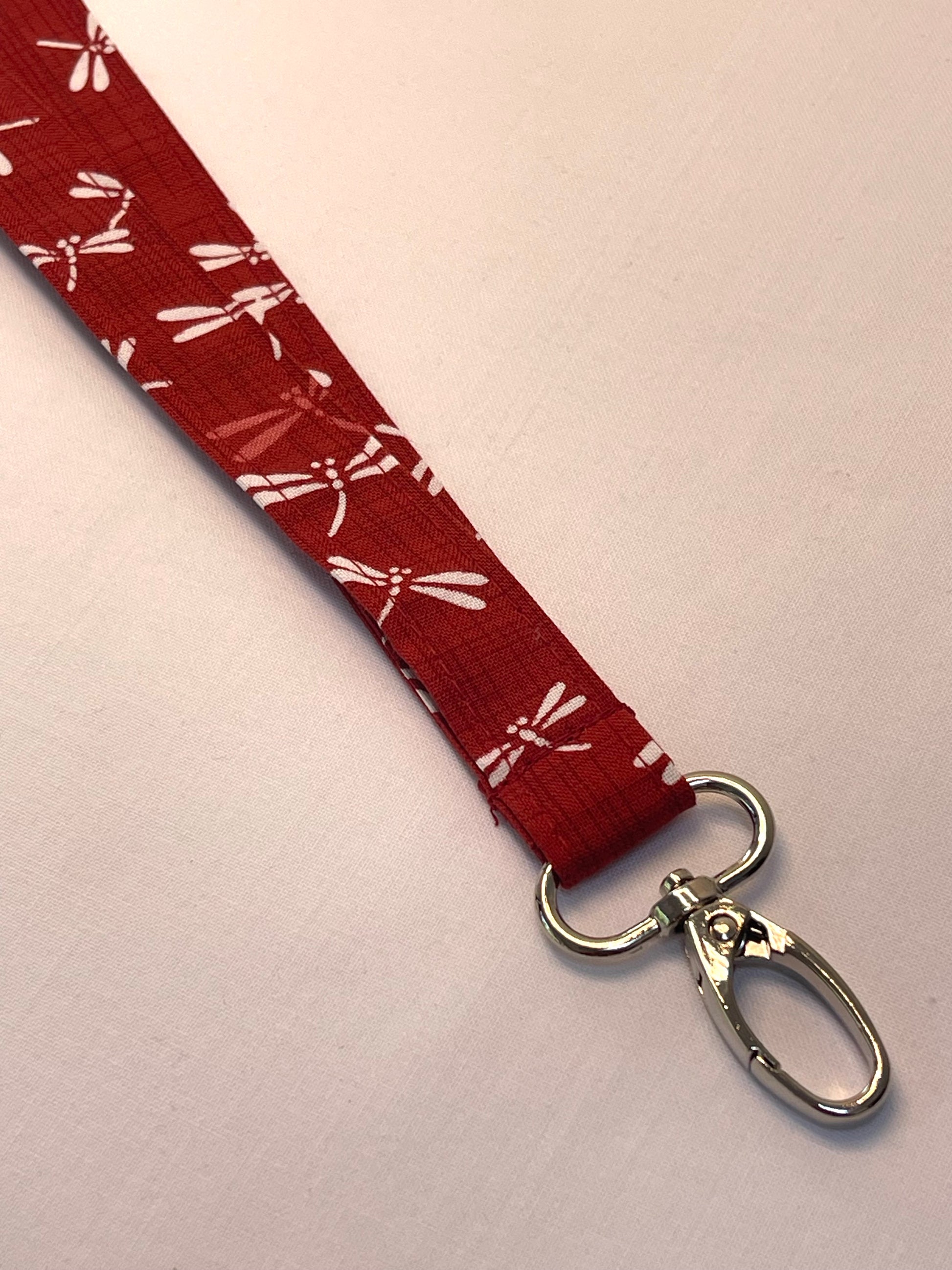 Red lanyard with white dragonfly pattern and metal clasp on a light pink background