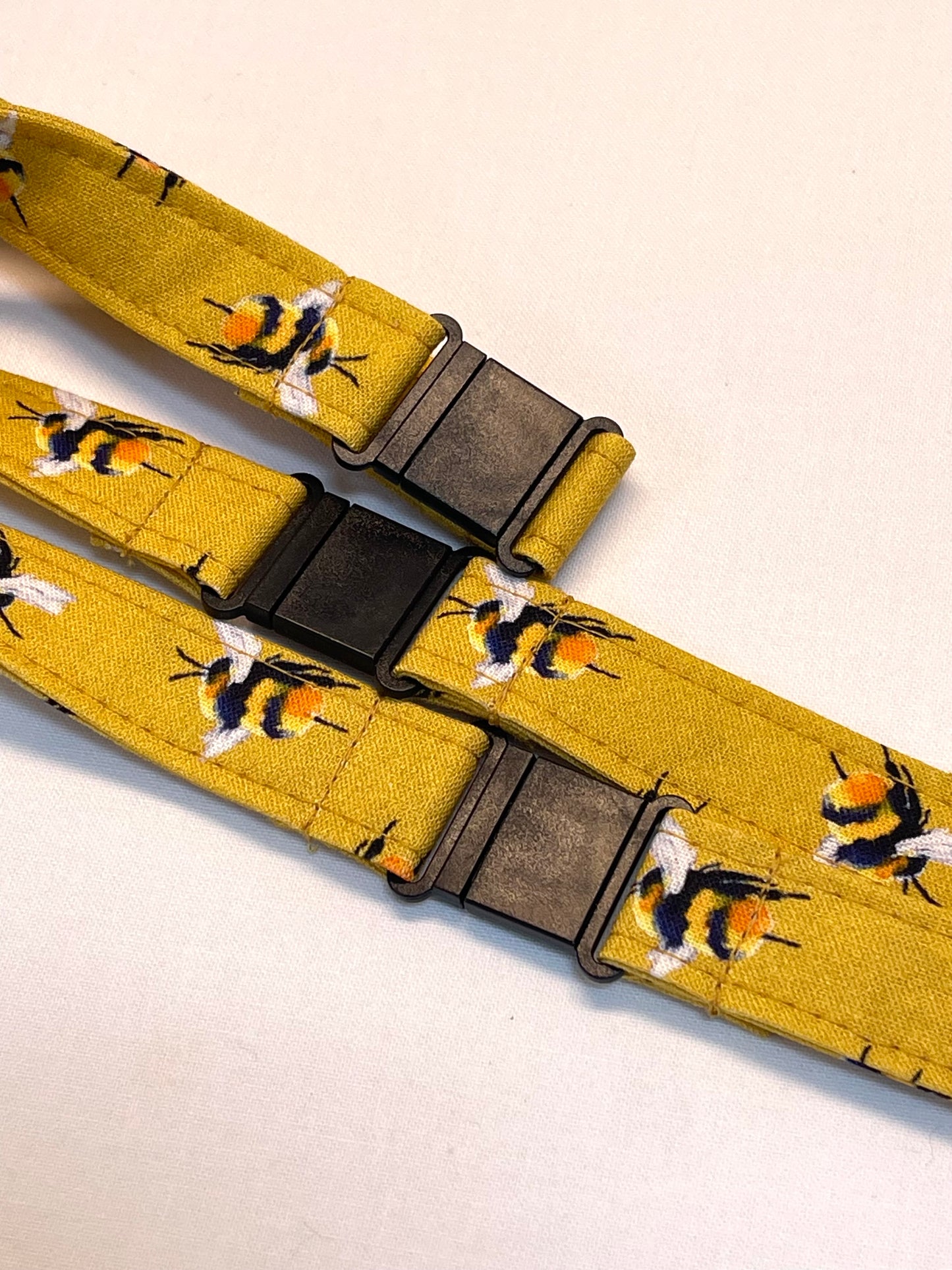Yellow lanyard with bee pattern and black breakaway clips on a light beige background
