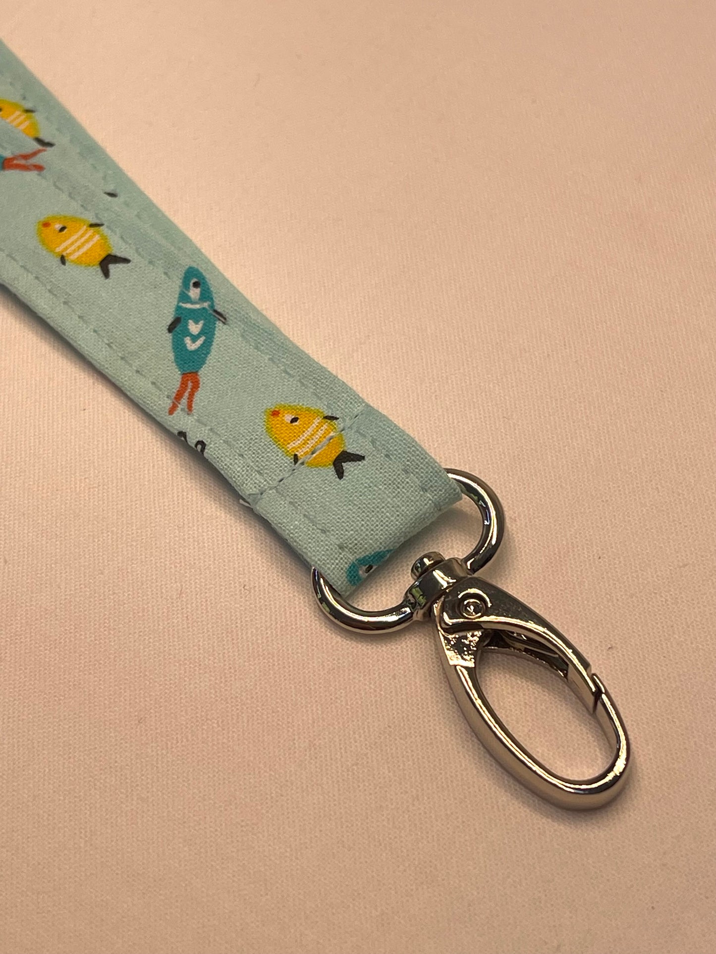 Fabric lanyard with fish pattern and metal clasp on a beige background